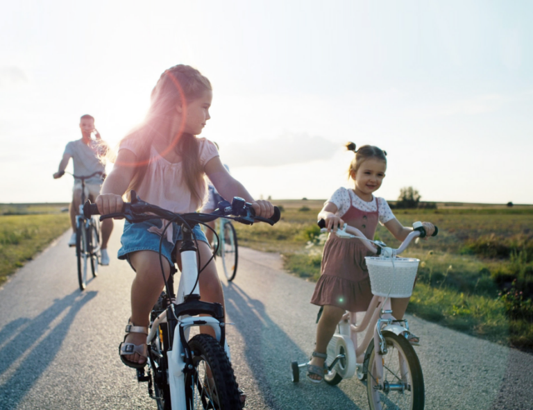 girls riding bicycles on a trail followed by their dad