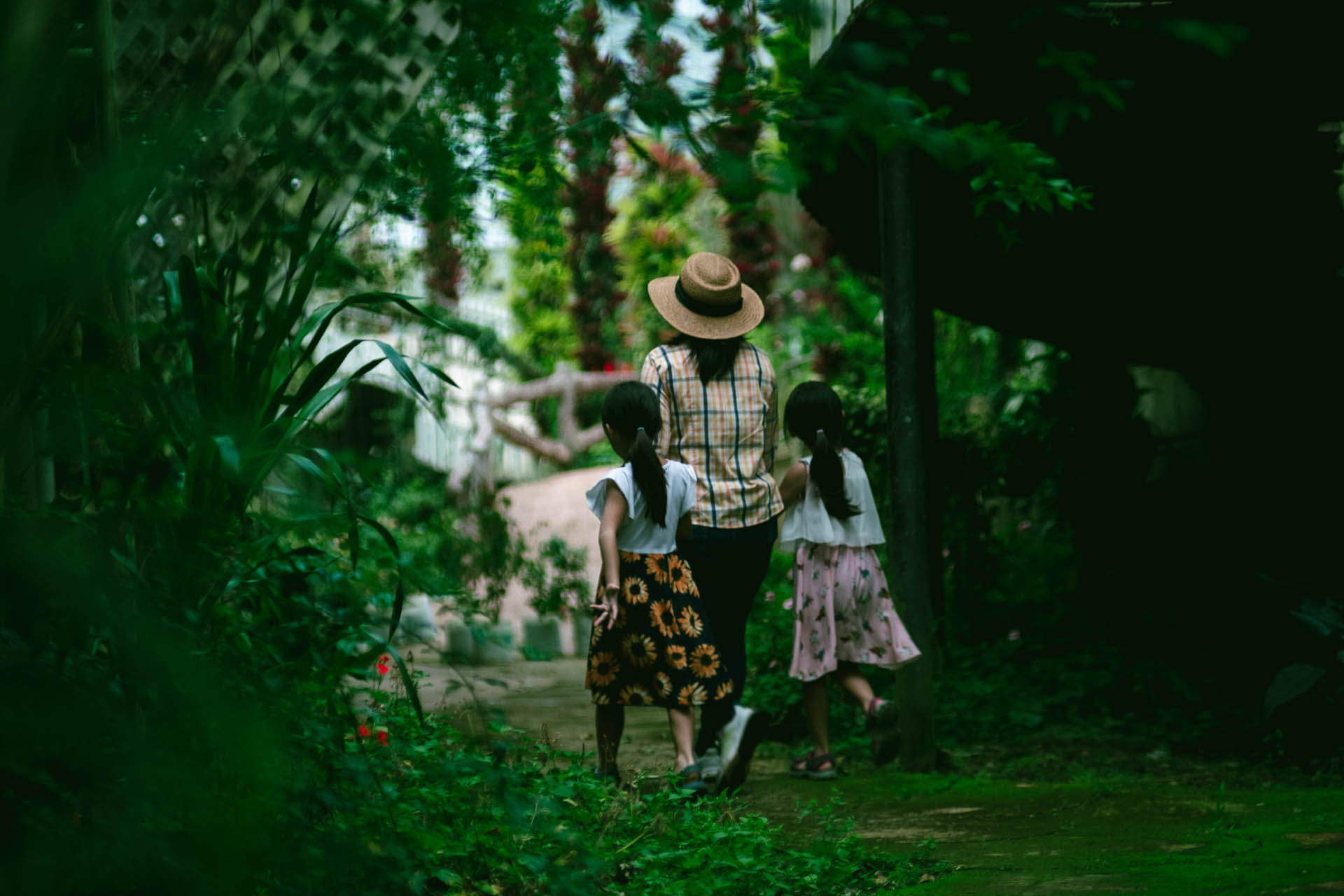 Lovely daughter and mother walking hand in hand on stone path in botanical garden with green plants and colorful flowers around.