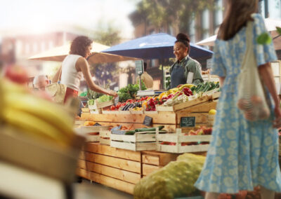 two women shop at a colorful farmers market stand while two shop purveyors smile and provide service - Orlando farm to table guide companion