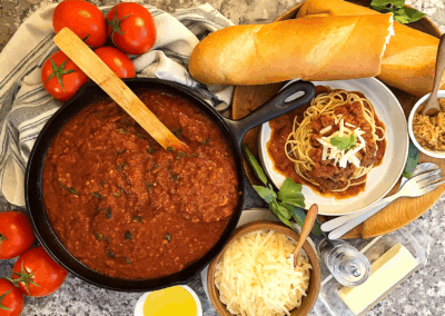 colorful image of Sunday gravy, Italian family-style, surrounded by tomatoes, bread, and cheese