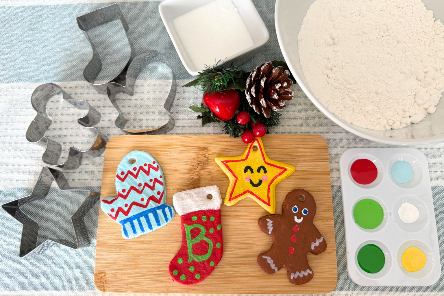 A vibrant image of supplies needed to make handmade salt dough ornaments, including flour, salt, cookie cutters, and paints, plus some completed ornaments